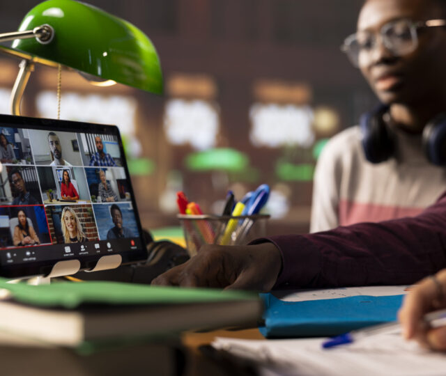 Group of diverse pupils engaging in an online course discussion via video call, participating at the remote class seminar from the campus library. Young people takes notes from academic tutor.